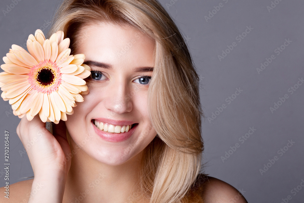 Beauty portrait of cheerful blonde woman with naked shoulders posing at studio with pink gerbera. Copy space Beauty portrait of cheerful blonde woman with naked shoulders posing at studio with pink gerbera. Copy space