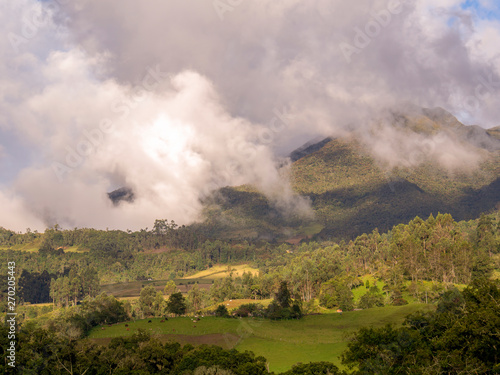 Panoramic view of the central Andean mountains of Colombia illuminated by the light of the sunset and covered with some dense clouds.