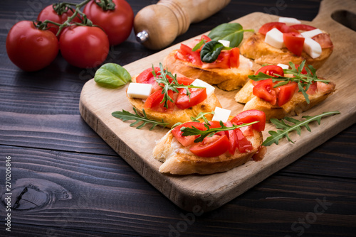 Bruschetta with tomatoes, mozzarella cheese and herbs on a cutting board in a dark background