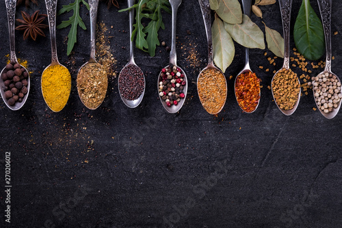 Spices and herbs on spoons in a black background, top view. Indian cuisine.