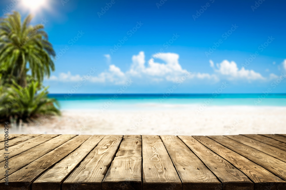 Wooden table background of free space and summer landscape of beach with palms and ocean. 