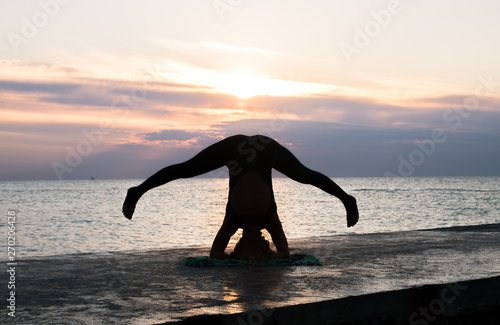 unrecognizable woman with beautiful body doing yoga headstand at sunrise on the sea, silhouette of yoga poses