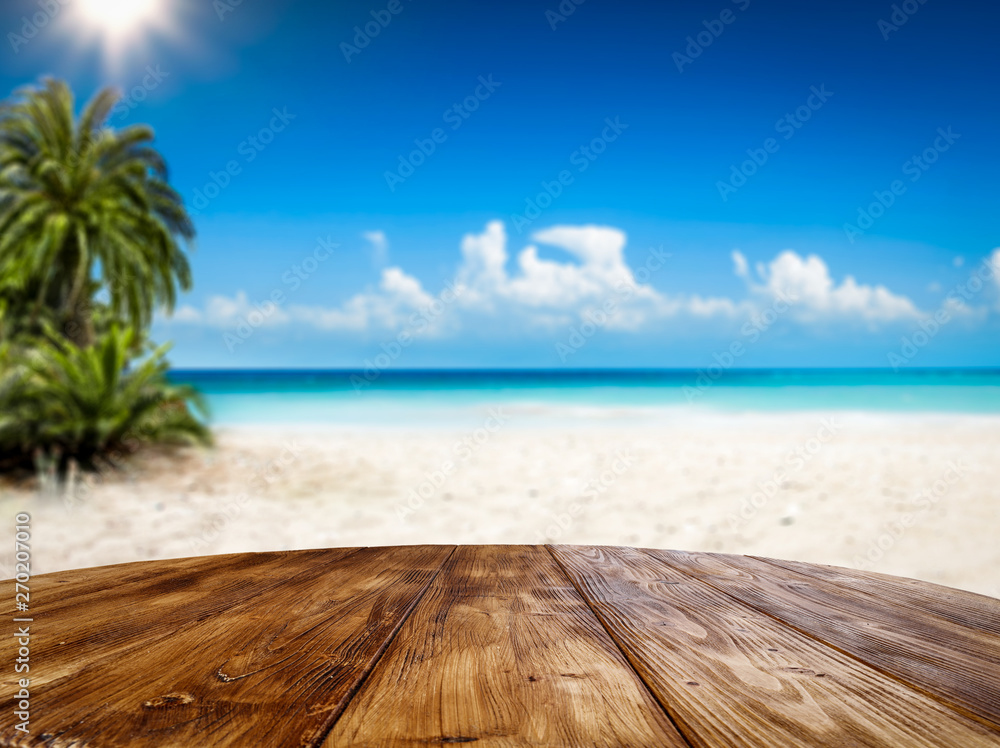 Fototapeta premium Wooden table background of free space and summer landscape of beach with palms and ocean.