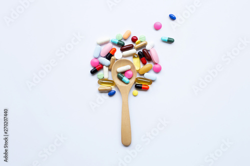 Colorful tablets, capsules and pills with wooden spoon on white