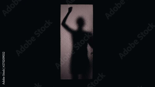 Dark silhouette of maniac catching female victim banging on glass door, crime