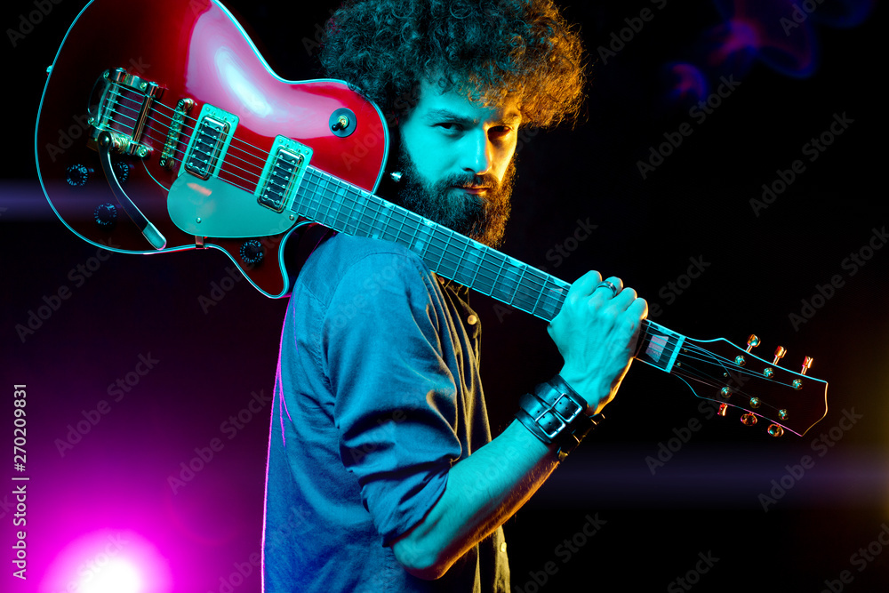 Obraz premium Close-up photo of hipster man with red guitar in neon lights. Rock musician is playing electrical guitar.