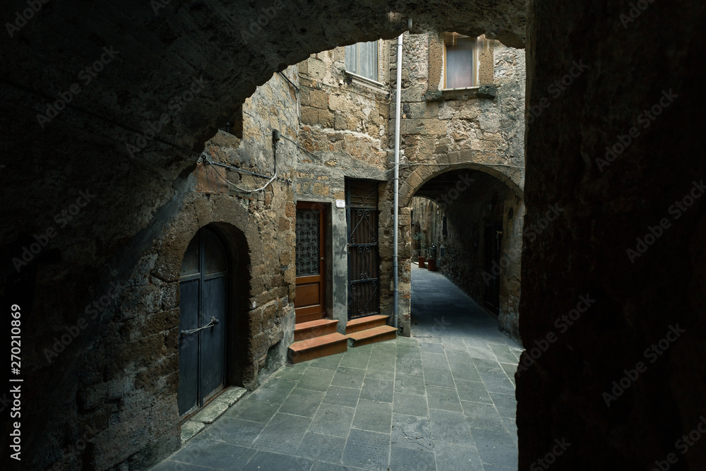 Dark alley leads to light with an arch in old medieval Italian town. Narrow street