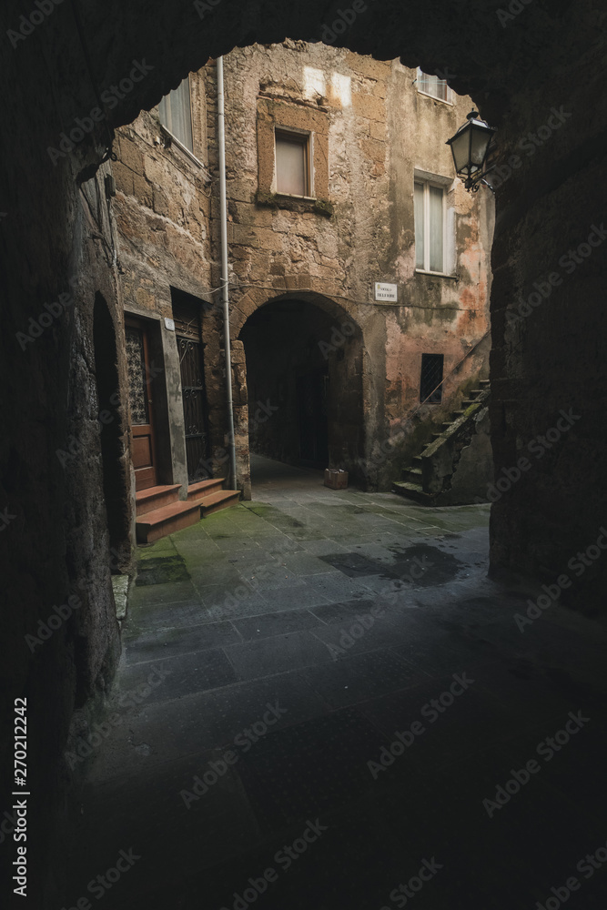Fototapeta premium Dark alley in old medieval town in Italy. Light in the distance of the narrow street
