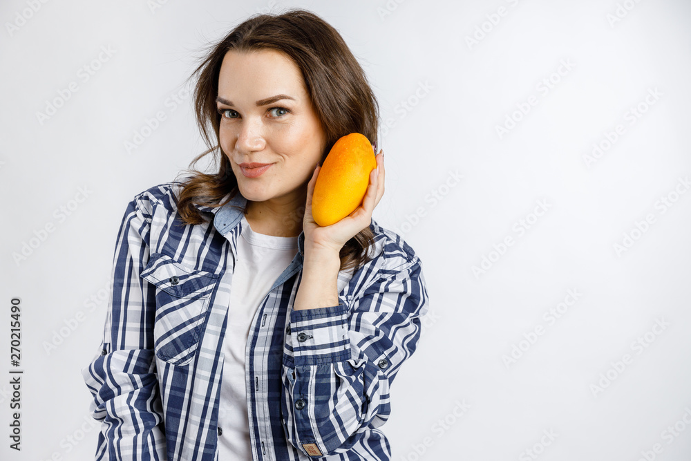 Young beautiful girl in plaid shirt holding mango on white background. Healthy food - vegetables, fruits and berries. Young beautiful girl in plaid shirt holding mango on white background. Healthy food - vegetables, fruits and berries.
