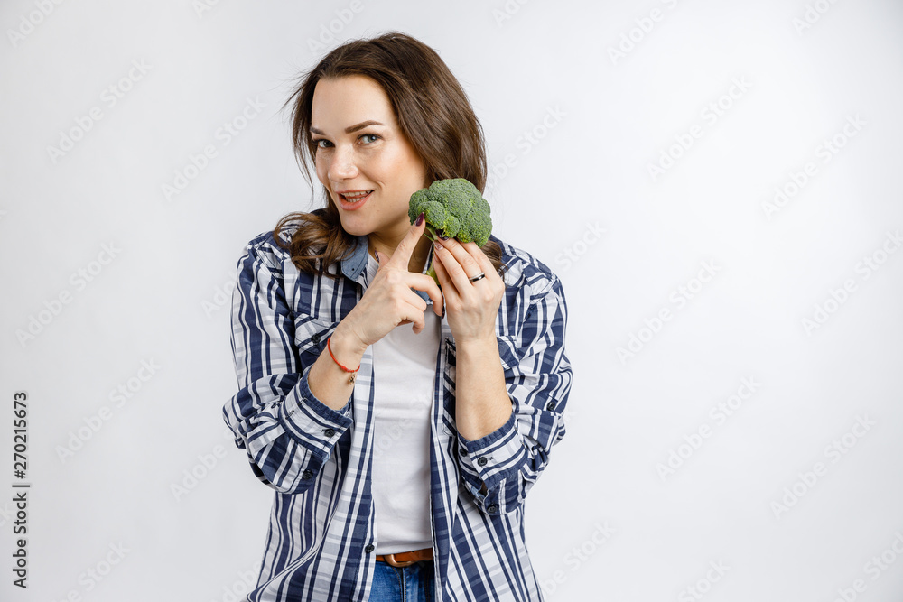 Young beautiful girl in plaid shirt holding broccoli on white background. Healthy food - vegetables, fruits and berries. Young beautiful girl in plaid shirt holding broccoli on white background. Healthy food - vegetables, fruits and berries.