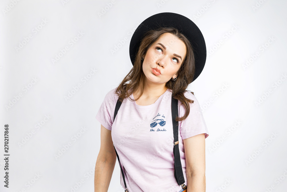Young beautiful girl posing in stylish black hat on white background. Emotions and gestures. Young beautiful girl posing in stylish black hat on white background. Emotions and gestures.