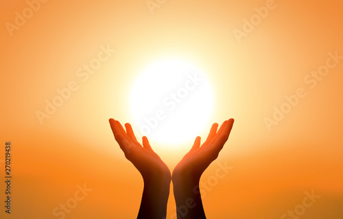 Free concept: Raised hands catching sun on sunset sky