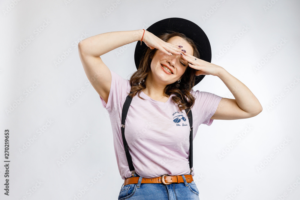 Young beautiful girl sitting on wooden chair in stylish black hat on white background. Emotions and gestures. Young beautiful girl sitting on wooden chair in stylish black hat on white background. Emotions and gestures.