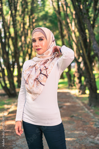 Young attractive Muslim Malay woman, modern contemporary fashion in hijab, close up portrait face and body, blurred background smiling and happy at park.