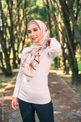 Young attractive Muslim Malay woman, modern contemporary fashion in hijab, close up portrait face and body, blurred background smiling and happy at park.