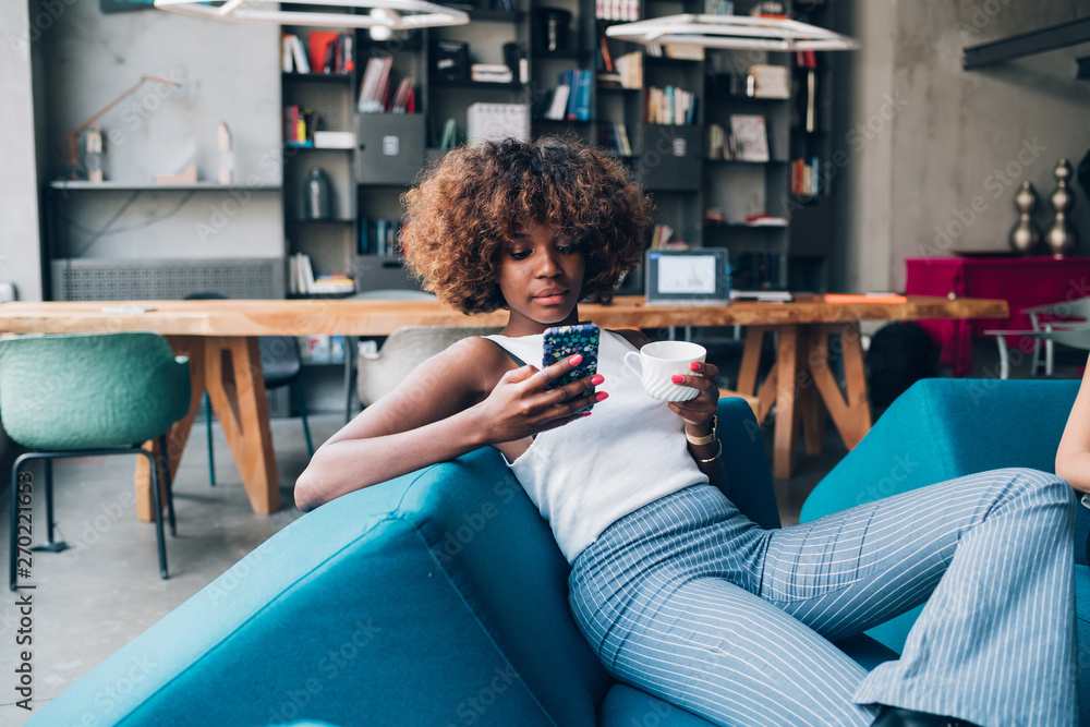 young black woman drinking and chatting with smartphone in modern loft young black woman drinking and chatting with smartphone in modern loft