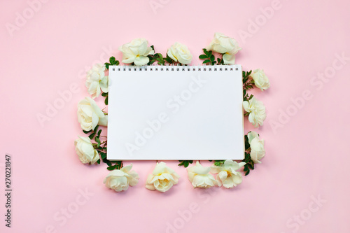 Floral frame of white roses around notebook on pastel pink background. copy space Birthday, Mother's, Valentines, Women's, Wedding Day concept.