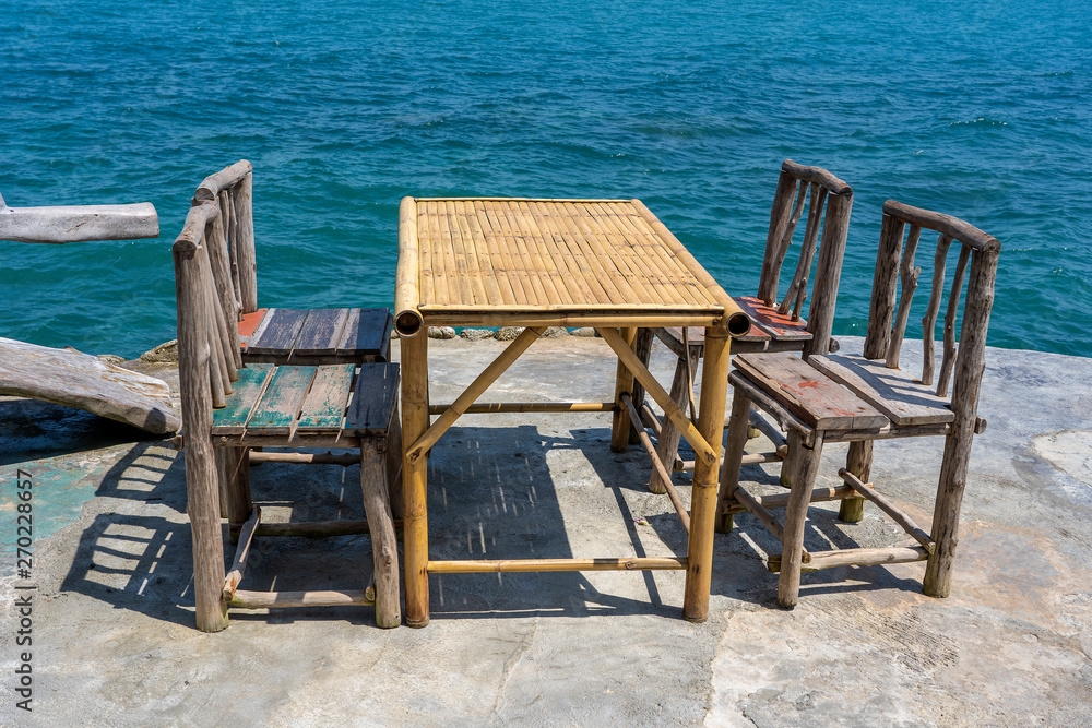Bamboo table and wooden chairs in empty cafe next to sea water in tropical beach . Island Koh Phangan, Thailand Bamboo table and wooden chairs in empty cafe next to sea water in tropical beach . Island Koh Phangan, Thailand