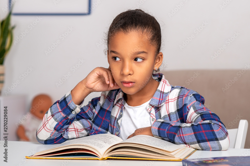 The schoolgirl sits at the table indoors and does his homework. The schoolgirl sits at the table indoors and does his homework.