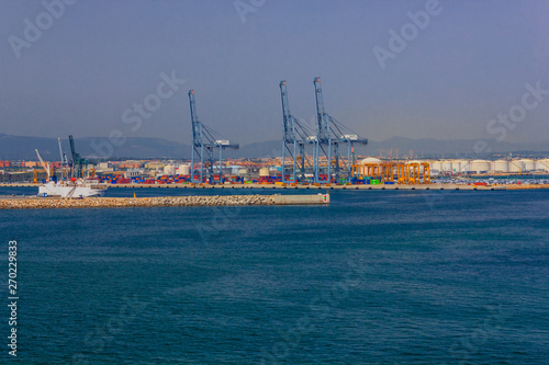 View of the commercial port of Tarragona in Spain with cranes to unload containers from merchant ships,  breakwater stones, and  the  warehouses for  storing goods  
