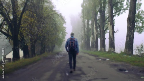 Wallpaper Mural Back view of young male traveler in jeans jacket with stylish backpack walking down the foggy deserted street. Travelling on foot. Adventure, hiking, active lifestyle. Slow motion Torontodigital.ca
