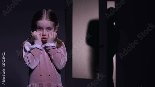 Terrified child closing eyes scary criminal silhouette entering room, kidnapping