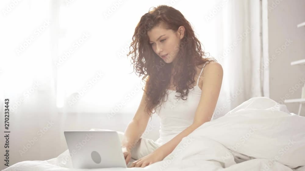 beautiful girl sitting on bed and using laptop at home in morning with sunlight beautiful girl sitting on bed and using laptop at home in morning with sunlight
