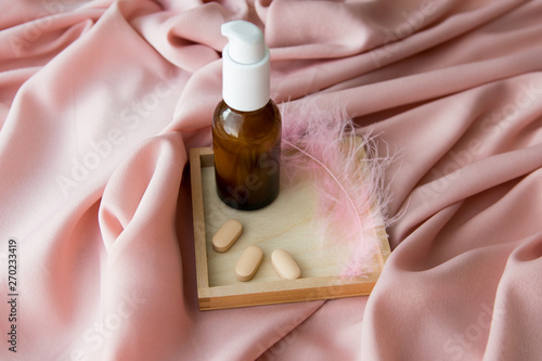 Pink feather with brown cream bottle, tablets on the texture table. photo