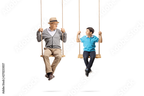 Senior man and boy sitting on swings and looking at each other