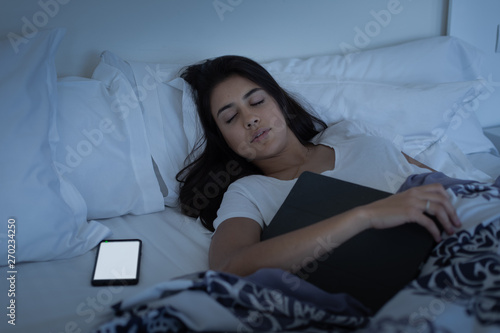 Millennial smartphone and tech addiction concept. Young woman falls asleep while using her mobile phone and tablet.
