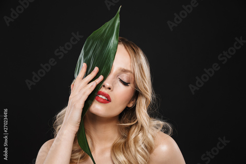 Beautiful woman with bright makeup red lips posing isolated over black background with leaf green flower.