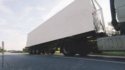 Cargo truck with cargo trailer driving on a highway. White Truck delivers goods in early hours of the Morning - very low angle drive thru close up shot.