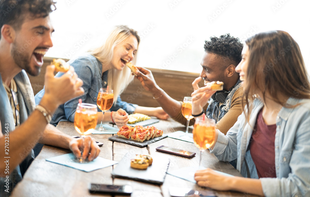 Friends eating and drinking spritz at fashion cocktail bar restaurant - Friendship concept with young people having fun together with drinks and food on happy hour at pub - Focus on pizza slices - obrazy, fototapety, plakaty 