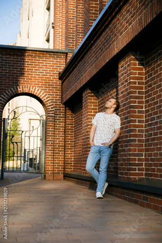 Young beautiful stylish man with bristles standing at the brick wall on a summer evening