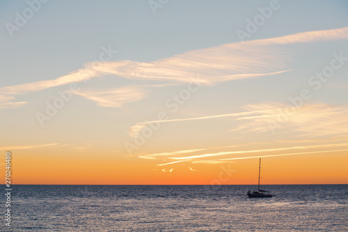 Lonely boat floats on a quiet warm calm sea against the backdrop of a golden sunset on a warm summer evening. Advertising space © Rithor