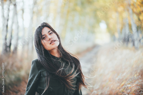 Dreamy beautiful girl with long natural black hair on bokeh background of autumn yellow leaves. Inspired girl enjoys nature in fall forest. Autumn euphoria. Female emotional portrait in faded tones.