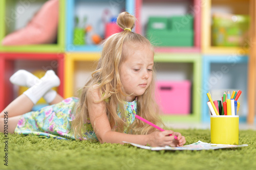 Portrait of cute little girl drawing at home on floor