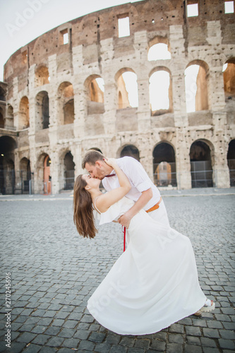 young beautiful couple in white clothes stands against the background of the Colosseum in Rome in Italy