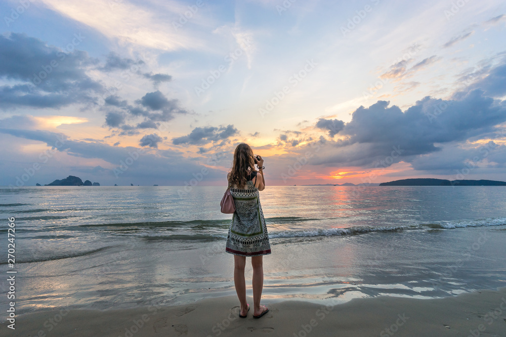 Tourist woman takes photo of colorful seascape at beautiful sunset with dramatic clouds on sky in Thailand