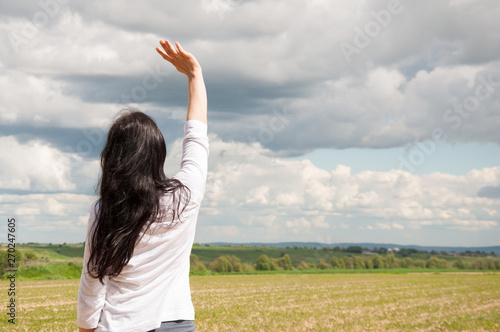 Fotografija A woman with her hands up on a green field praises God