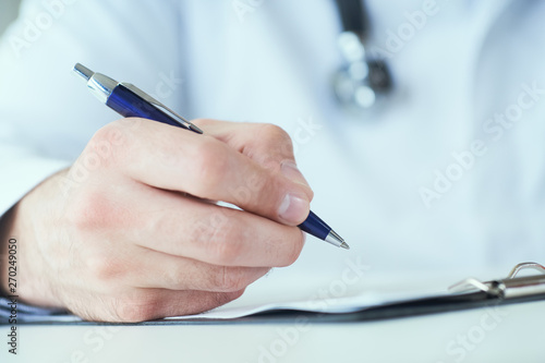 Male physician medicine doctor or pharmacist writing prescription on special form sitting at worktable. Medical care  pharmacy or health insurance concept.
