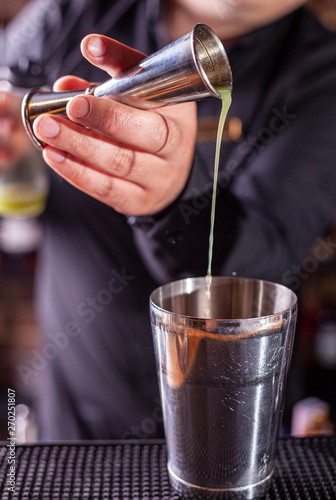 barman preparing cocktai and pours liquid into the jigger in a cocktail bar