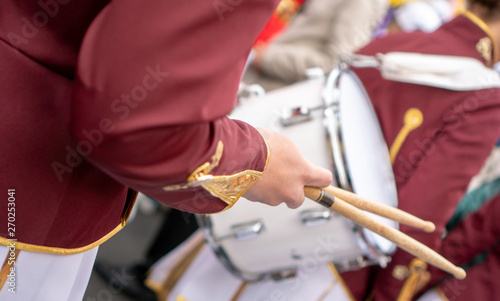 Orchestral drummer in a claret-white uniform with a white drum and drum sticks