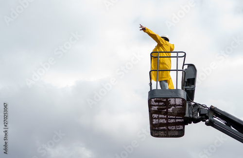 The builder in a yellow raincoat on cherry picker indicates the direction