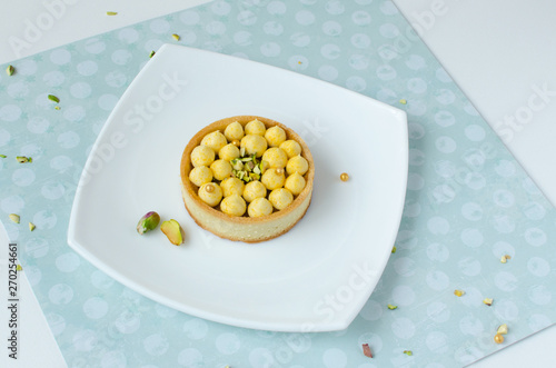 Modern tart with tropical flavor decorated with pistachio on white plate on green background