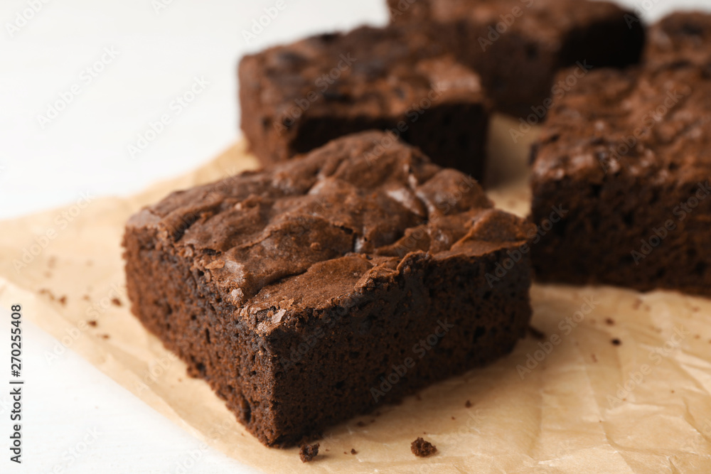 Parchment paper with fresh brownies on white table, closeup. Delicious chocolate pie Parchment paper with fresh brownies on white table, closeup. Delicious chocolate pie