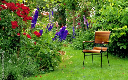 Green garden idyll with red roses and a stylish chair.