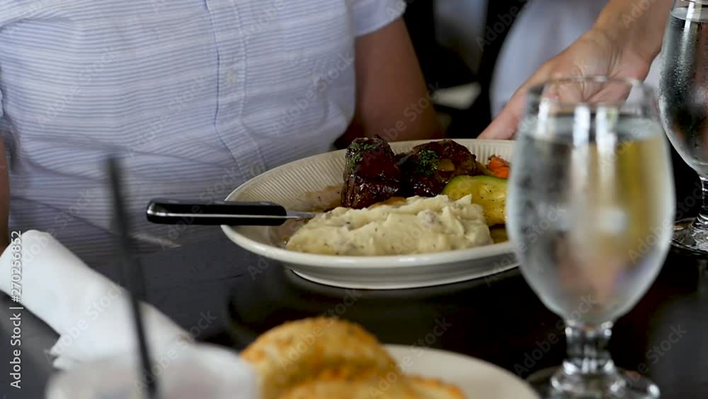 waitress places stake and potato dish in front of man slow motion. A waitress sets a plate of steak and potatoes in front of a man at a restaurant table. You can see a cold glass of water. waitress places stake and potato dish in front of man slow motion. A waitress sets a plate of steak and potatoes in front of a man at a restaurant table. You can see a cold glass of water.