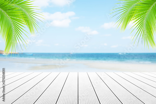 Empty wooden table or dock floor and palm leaves with blurred background, beach and beautiful sea in daytime.