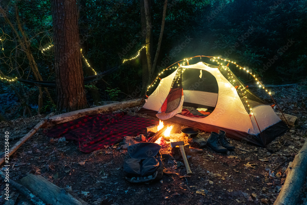 Camping tent in the Blue Ridge Mountains in Asheville, North Carolina.  Outdoor lifestyle with axe, cast iron skillet, flannel blanket. Rustic Bushcraft  Campsite. Survival shelter in the wilderness. Stock Photo